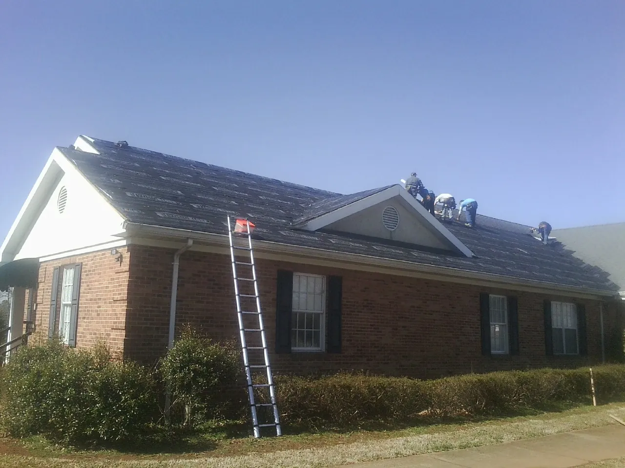 Crew tearing shingles off a brick ranch roof with a ladder set — Emergency Roof Repair work by our crew in Lumberville