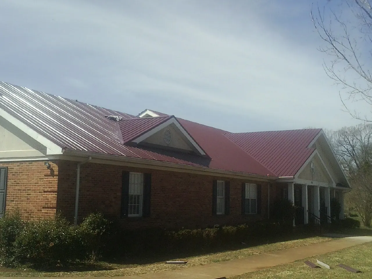 Red metal roof with gabled entries on a long brick building, from a Hail Damage Roof Repair job in Lumberville