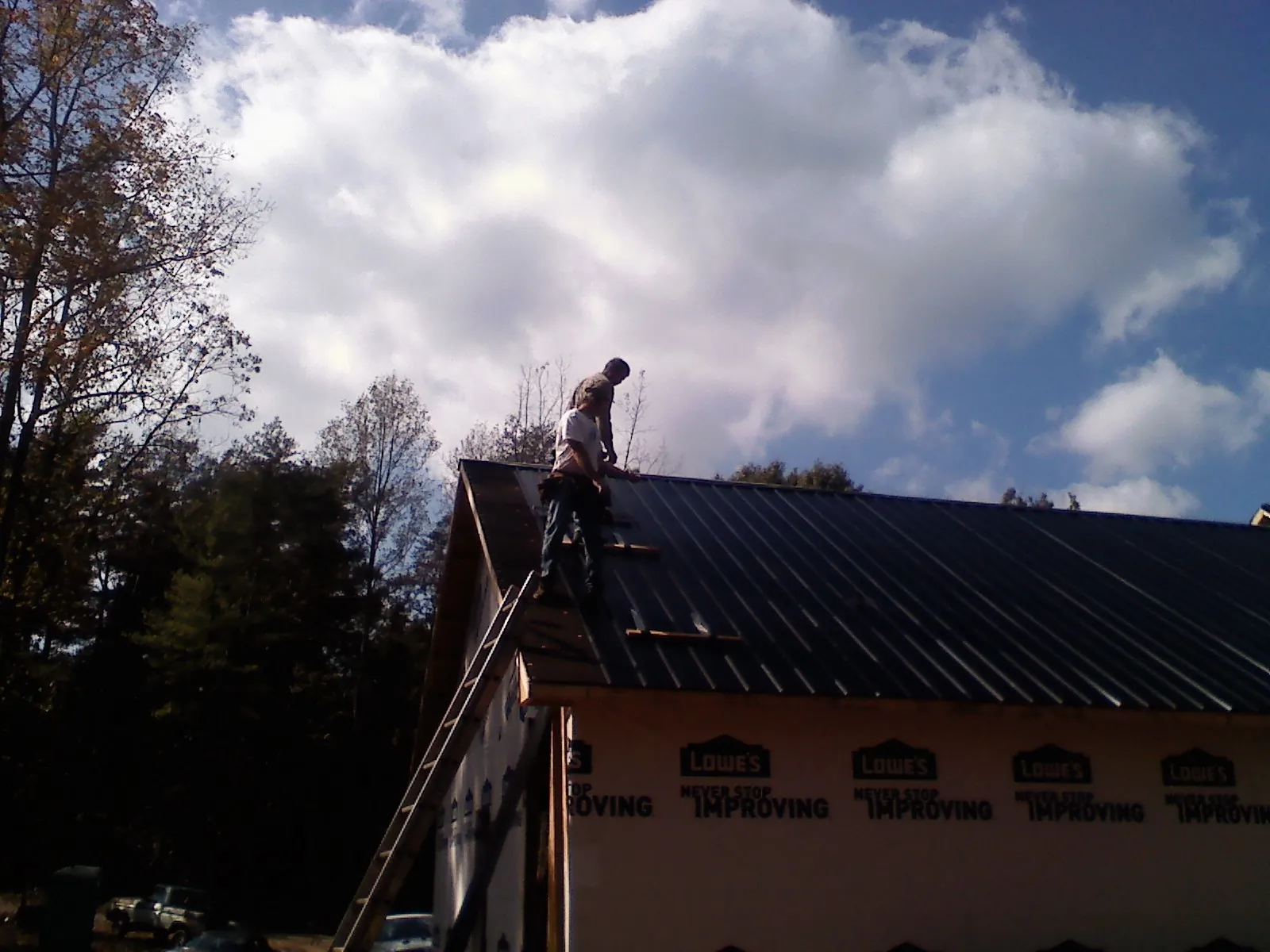 Roofer fastening dark metal panels high against a cloudy sky, from a Roof Inspection job in Lumberville