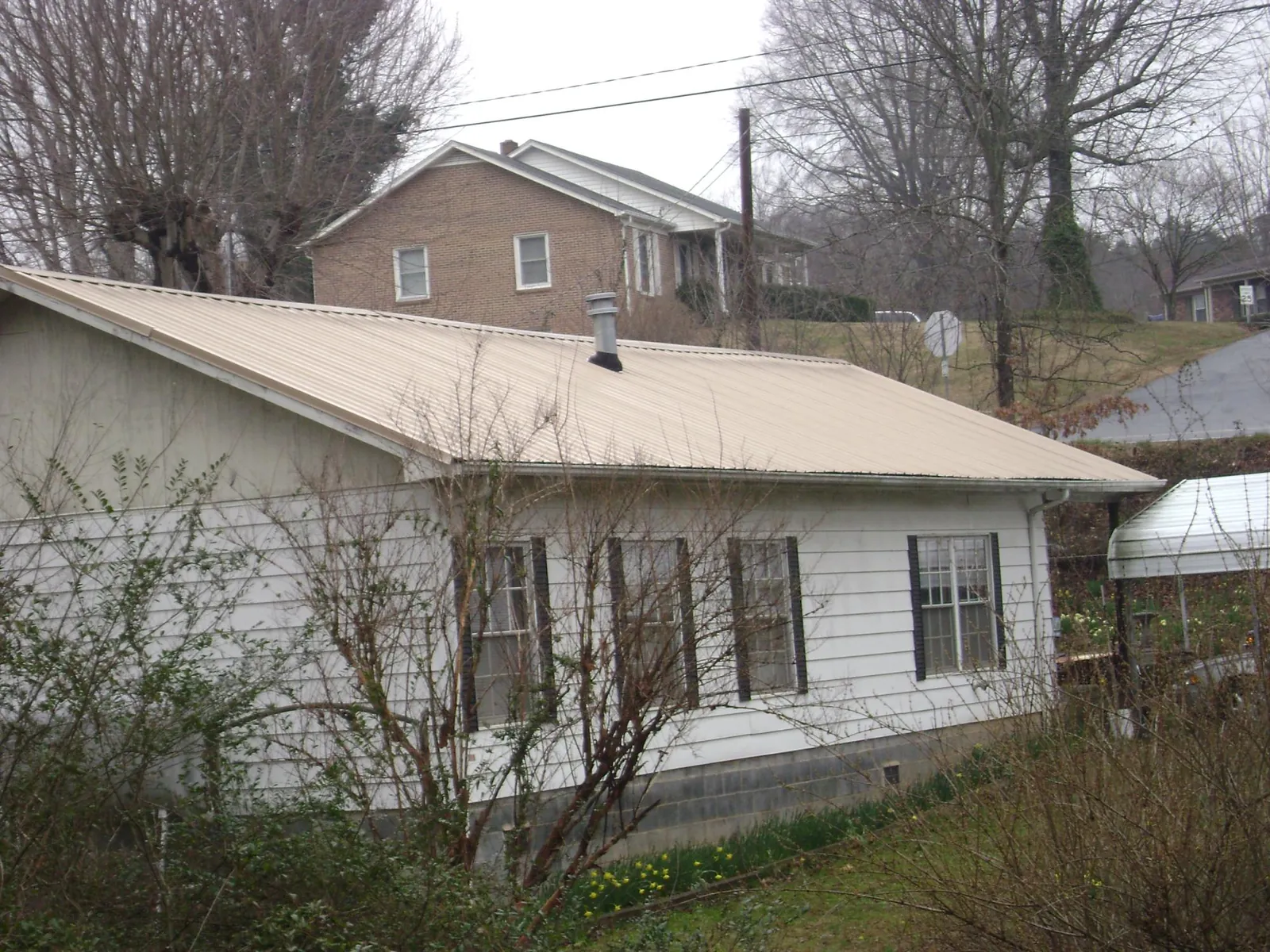 Tan metal roof on a white sided house set into a hillside — Commercial Roofing by Roofing Brothers in Lumberville